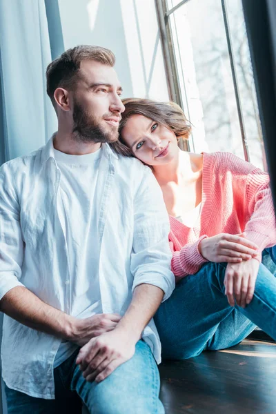 Fröhliche brünette Frau sitzt am Fenster mit hübschem Mann zu Hause — Stockfoto