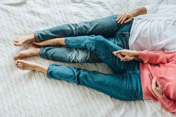 Vista cortada de homem e mulher de mãos dadas e deitado na cama — Fotografia de Stock