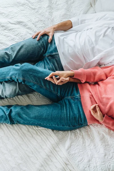 Обрезанный вид мужчины и женщины, держащихся за руки, когда они лежат на кровати — стоковое фото