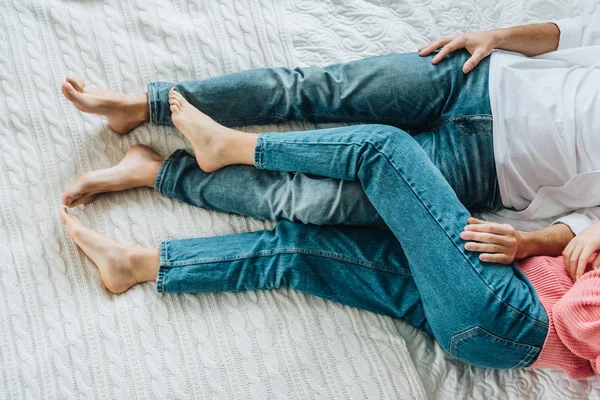 Cropped view of man and woman in jeans lying on bed — Stock Photo