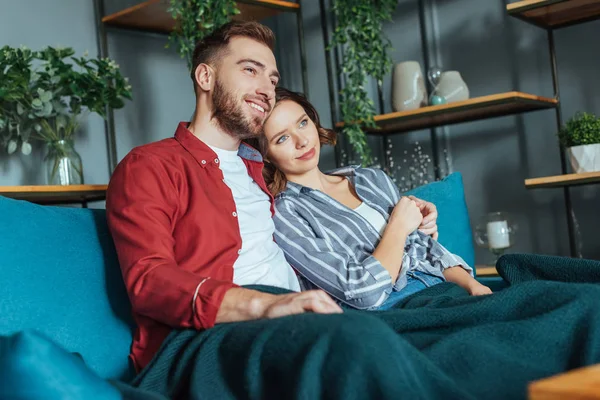 Hombre feliz abrazando a mujer atractiva mientras está sentado en el sofá en casa - foto de stock