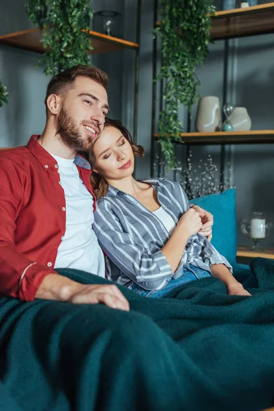 Homem feliz abraçando mulher atraente com olhos fechados enquanto sentado no sofá em casa — Fotografia de Stock