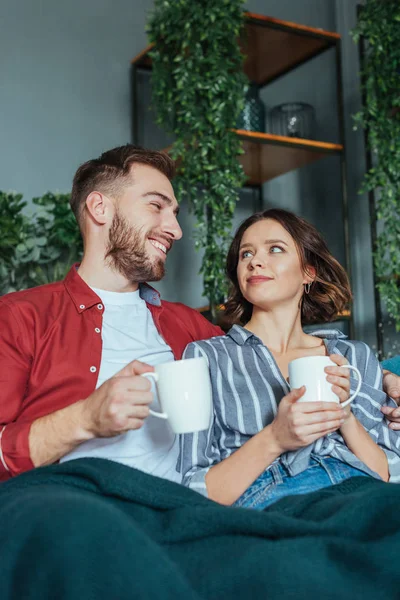 Vista de ángulo bajo de hombre alegre mirando mujer atractiva con taza de café - foto de stock