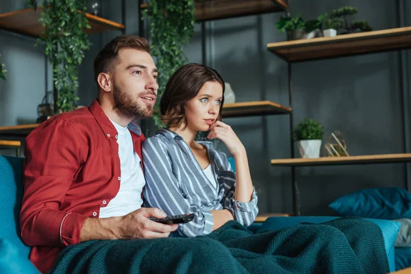 Bel homme tenant télécommande tout en regardant un film avec une femme à la maison — Photo de stock