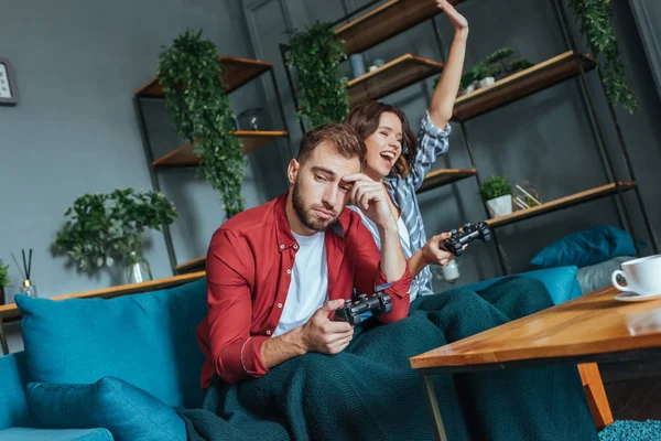 Low angle view of upset man near happy brunette woman celebrating and gesturing in living room — Stock Photo