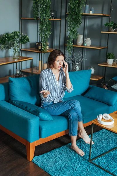 Chateado mulher gestos ao falar no smartphone na sala de estar — Fotografia de Stock