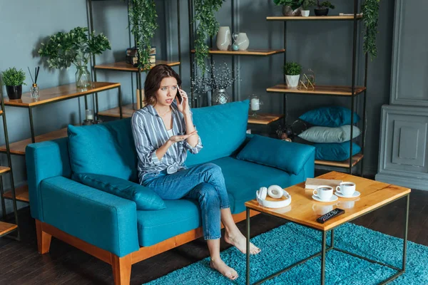 Frustrierte Frau gestikuliert, während sie im Wohnzimmer mit dem Smartphone spricht — Stockfoto