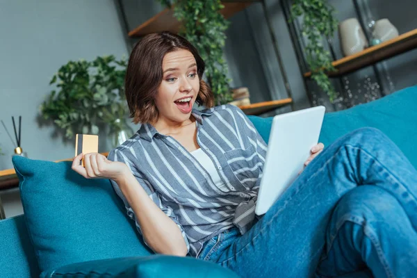Low angle view of surprised woman looking at digital tablet while holding credit card — Stock Photo