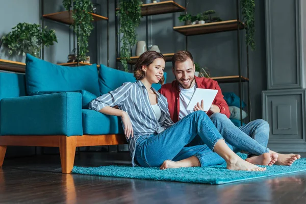 Vista de ángulo bajo de hombre y mujer feliz mirando tableta digital en la sala de estar - foto de stock