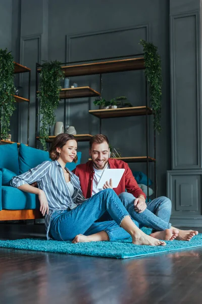 Низкий угол зрения счастливого мужчины и веселой женщины, смотрящей на цифровой стол в гостиной — стоковое фото