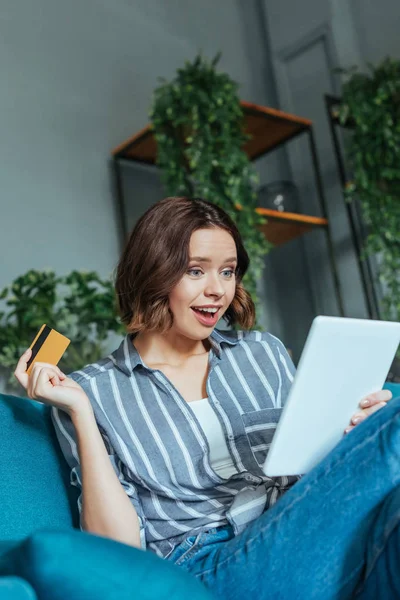 Niedrigwinkel-Ansicht einer überraschten Frau, die auf ein digitales Tablet blickt, während sie ihre Kreditkarte hält — Stockfoto