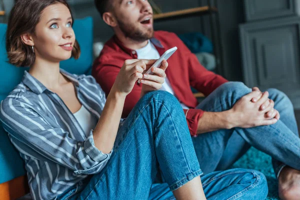 Selective focus of attractive woman holding smartphone near surprised man — Stock Photo