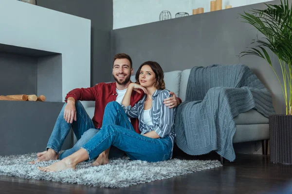 Homem feliz sorrindo enquanto sentado no tapete com bela mulher morena — Fotografia de Stock