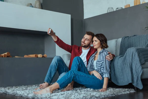 Feliz hombre sonriendo mientras toma selfie con hermosa mujer morena - foto de stock