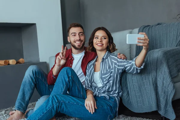 Donna allegra prendendo selfie con uomo felice mostrando segno di pace — Foto stock