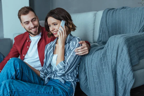 Enfoque selectivo de la mujer alegre hablando en el teléfono inteligente cerca del hombre guapo - foto de stock