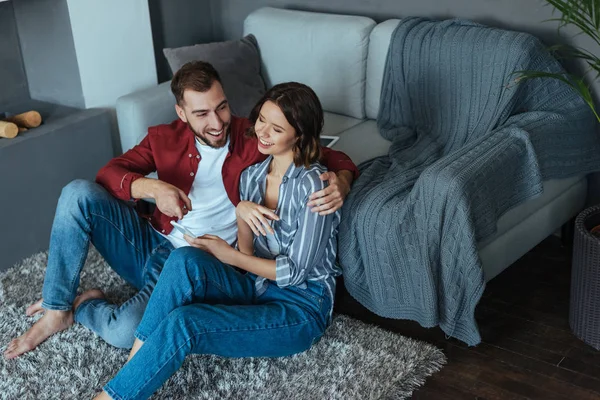 Blick von oben auf einen gut aussehenden Mann, der eine lächelnde Frau ansieht, während er sein Smartphone in der Hand hält — Stockfoto