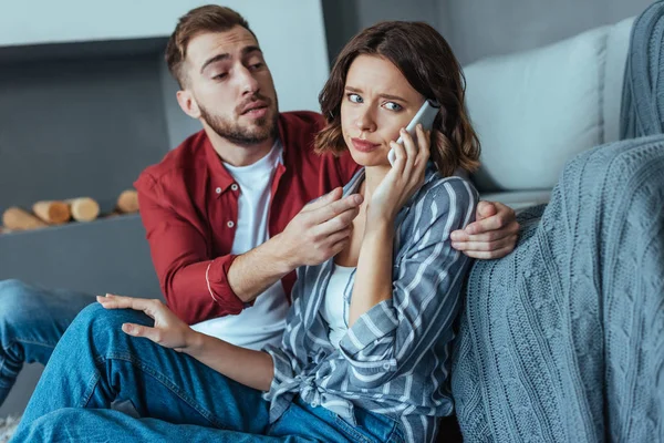 Bärtiger Mann schaut aufgebrachte Frau an, die zu Hause auf Smartphone spricht — Stockfoto