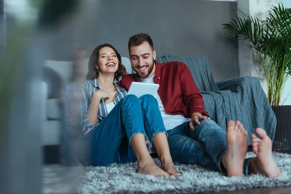 Selektiver Fokus einer fröhlichen Frau, die lacht, während sie ein digitales Tablet in der Nähe eines glücklichen Mannes hält — Stockfoto