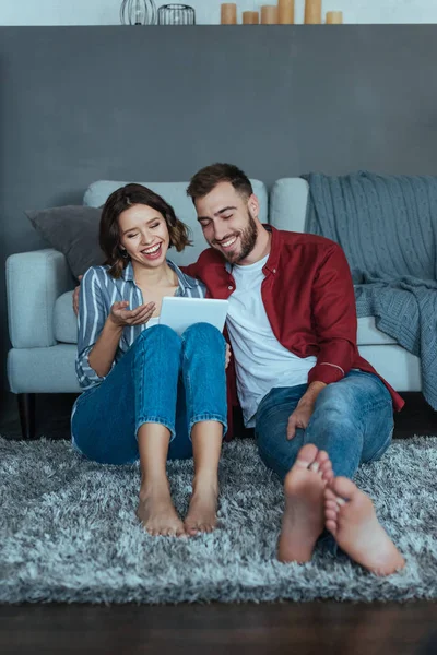 Fröhliche Frau gestikuliert beim Blick auf digitales Tablet neben glücklichem Mann — Stockfoto