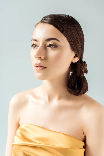 Mujer joven con labios brillantes y sombra de ojos dorada mirando hacia otro lado aislado en gris - foto de stock