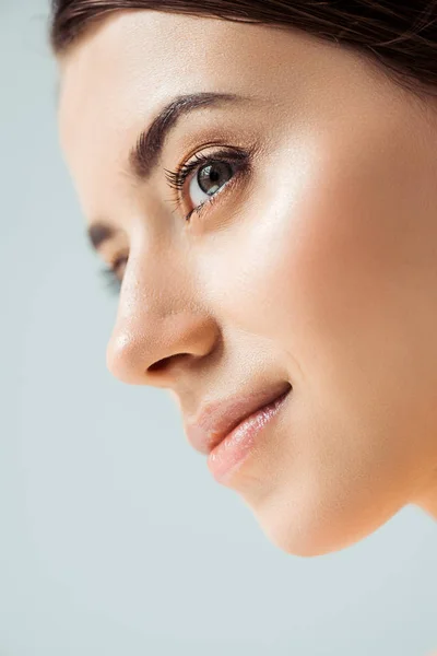 Primer plano de joven mujer sonriente con labios brillantes y sombra dorada de ojos aislada en gris - foto de stock