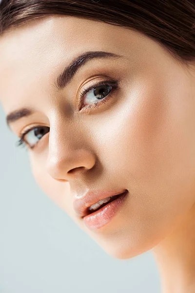 Joven hermosa mujer con labios brillantes y sombra de ojos dorados mirando a la cámara aislada en gris - foto de stock