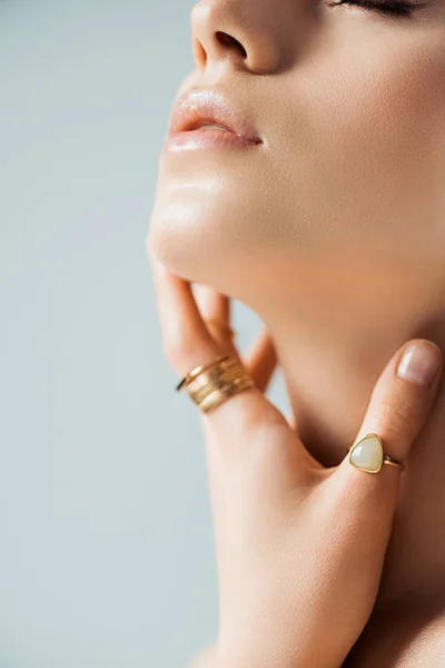 Vista recortada de mujer joven en anillos de oro tocando cuello aislado en gris — Stock Photo