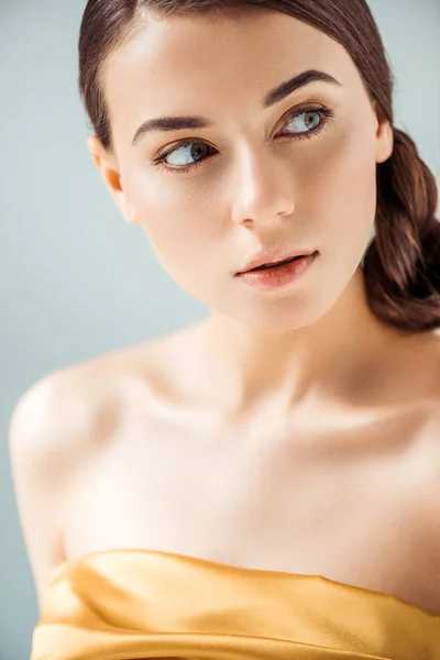 Mujer joven soñadora con labios brillantes y sombra de ojos dorada mirando hacia otro lado aislado en gris - foto de stock