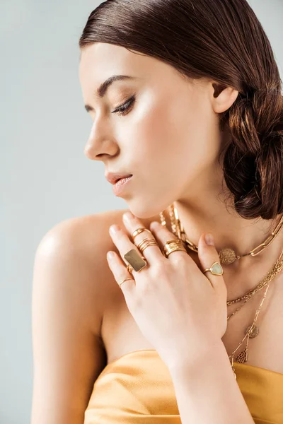 Mujer joven con maquillaje brillante en collares dorados y anillos aislados en gris - foto de stock