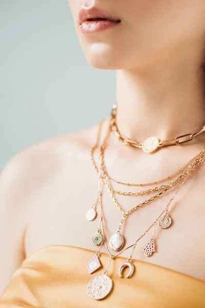 Vista recortada de mujer joven con labios brillantes en collares dorados aislados en gris - foto de stock