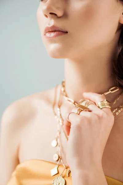 Vista parcial de mujer joven con labios brillantes en collares dorados y anillos aislados en gris - foto de stock