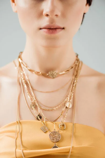 Частичный вид молодой женщины с блестящими губами в золотых ожерельях, изолированных на сером — стоковое фото