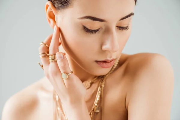 Young naked woman with shiny makeup in golden necklaces and rings isolated on grey — Stock Photo