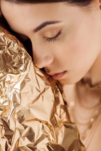 Joven hermosa mujer con maquillaje brillante y lámina de oro posando con los ojos cerrados - foto de stock