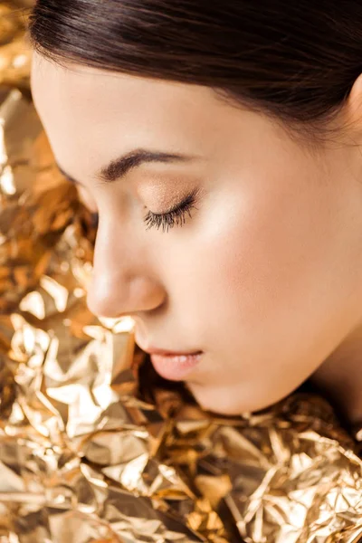 Портрет молодої жінки з блискучим макіяжем біля золотої фольги, позує закритими очима — стокове фото