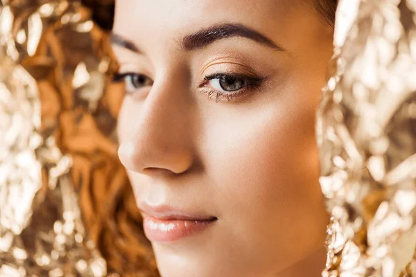 Portrait of young attractive woman with shiny makeup near golden foil — Stock Photo