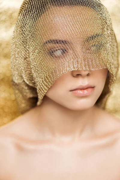Giovane donna nuda con labbra lucide e panno dorato sul viso guardando lontano su sfondo oro strutturato — Foto stock