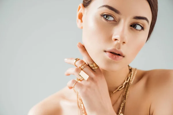 Mujer desnuda joven en anillos de oro y collares mirando hacia otro lado aislado en gris - foto de stock