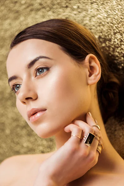 Junge nackte schöne Frau mit glänzendem Make-up in goldenen Ringen auf goldenem strukturiertem Hintergrund — Stockfoto