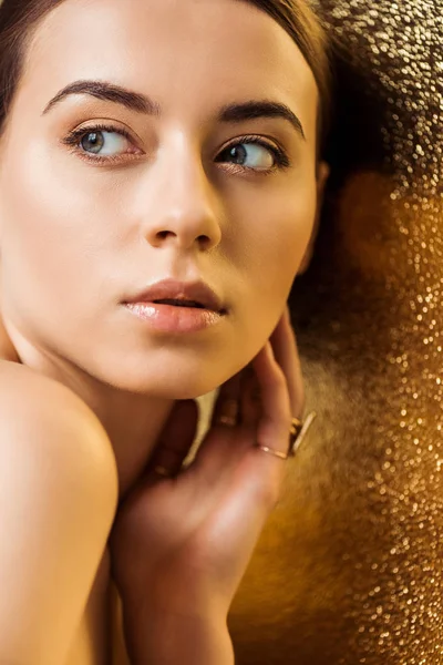Mujer joven atractiva desnuda con maquillaje brillante y anillos de oro sobre fondo de textura dorada - foto de stock