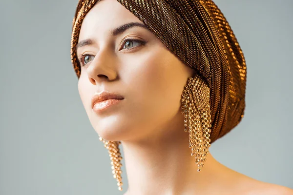Jovem mulher nua com maquiagem brilhante, anéis dourados em turbante olhando para longe isolado em cinza — Fotografia de Stock
