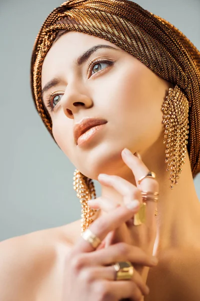 Mujer desnuda joven con maquillaje brillante, anillos de oro y pendientes en turbante aislado en gris - foto de stock