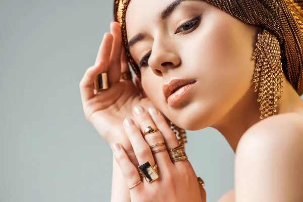 Jovem mulher nua concurso com maquiagem brilhante, anéis dourados e brincos em turbante isolado em cinza — Fotografia de Stock