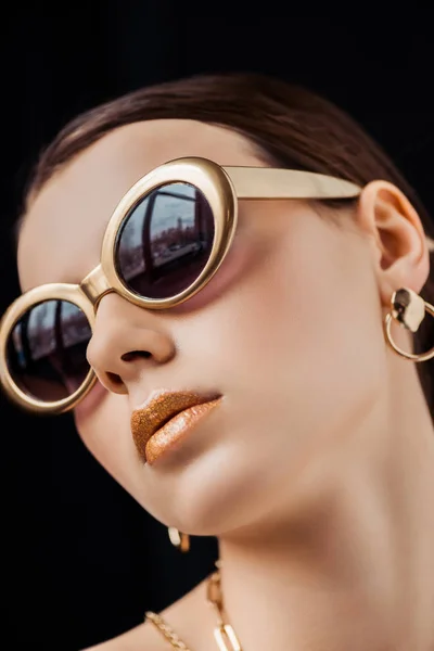 Mujer joven en gafas de sol, pendientes de oro y collares aislados en negro - foto de stock