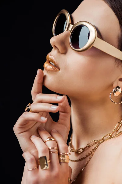 Mujer desnuda joven en gafas de sol, pendientes de oro, anillos y collares aislados en negro - foto de stock