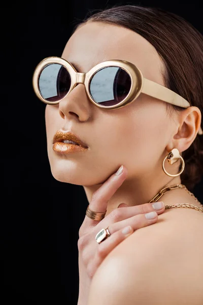 Young naked woman in sunglasses and golden jewelry isolated on black — Stock Photo