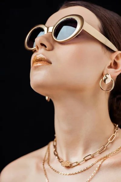 Jovem mulher nua atraente em óculos de sol e jóias de ouro isolado em preto — Fotografia de Stock