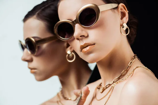 Jeune femme nue en lunettes de soleil, bijoux dorés tenant miroir isolé sur noir — Photo de stock