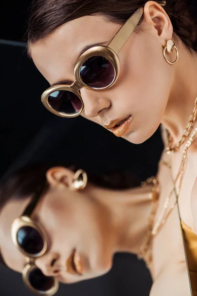 Young stylish woman in sunglasses, golden jewelry holding mirror near face — Stock Photo